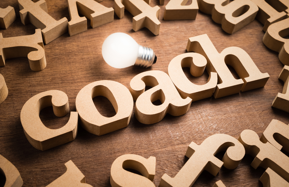 Das Wort "Coach" aus Holzbuchstaben gelegt, mit Glühbirne