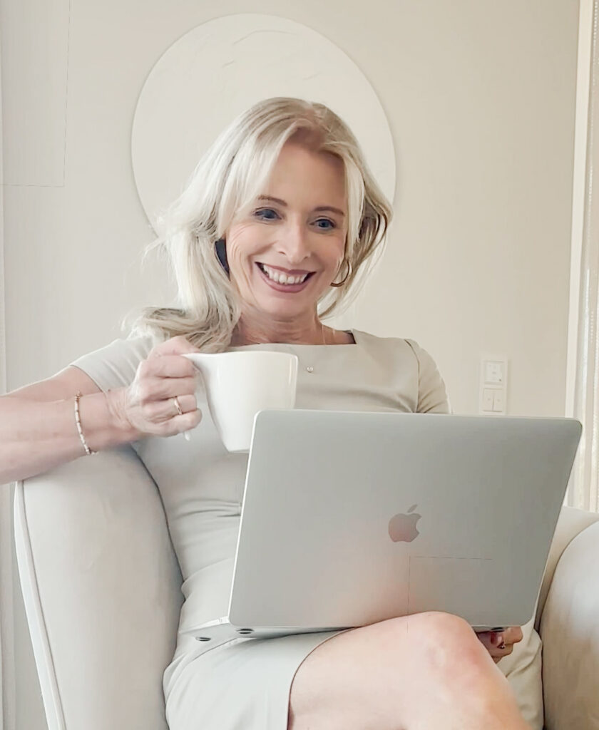 Christina Soltau sitzt auf Sessel, hat einen Laptop auf dem Schoß und ist in einer Videobesprechung. Sie hält eine Tasse in ihrer Hand.